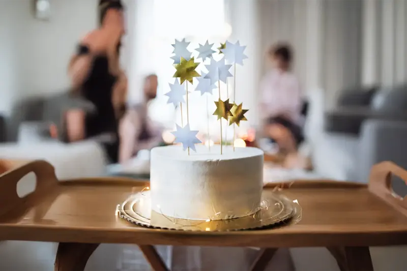 A white birthday cake topped with gold and silver stars on a wooden serving tray