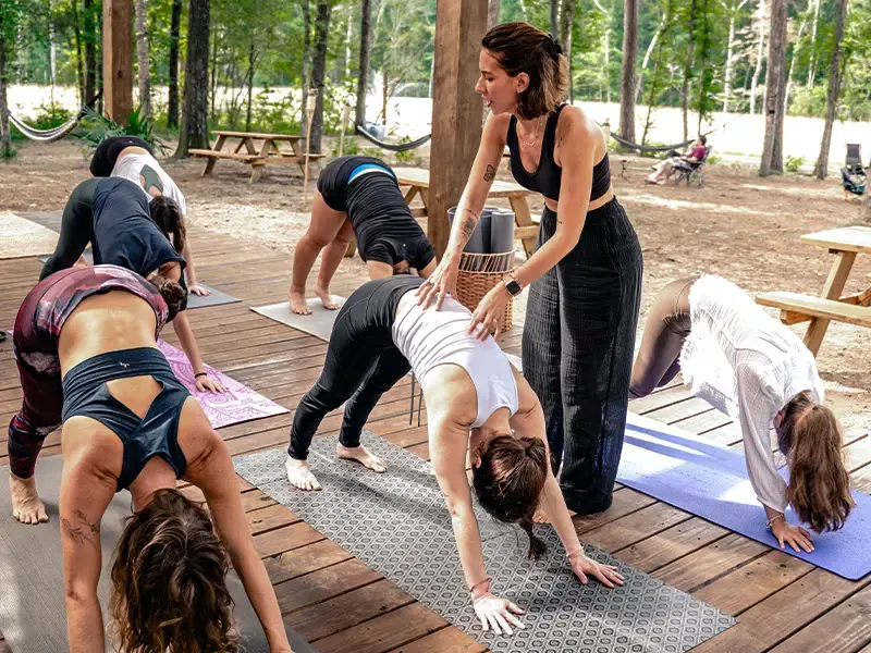 An instructor guiding a group through a downward dog pose on an outdoor wooden deck among the pines