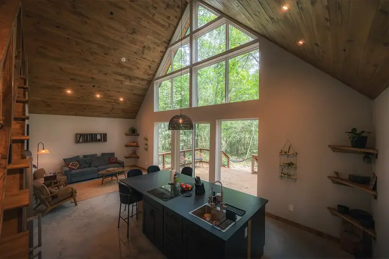 Two-story great room with a wall of forest-facing windows, a kitchen island and a sofa