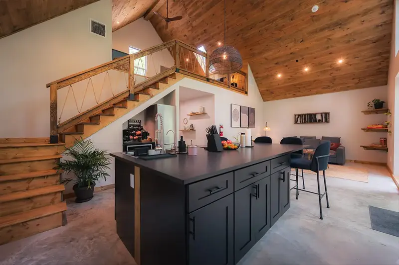 Kitchen island with bar stools beside a wooden staircase with rope railings up to the loft